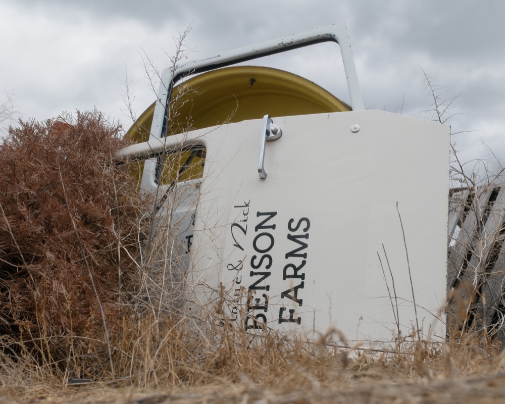 A weathered Benson Farms nameplate resting in dry brush